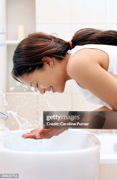 young woman splashing water on face in bathroom - girls taking a showering stockfoto's en -beelden