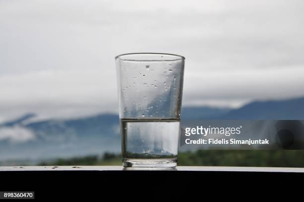 a mountain range and sky scenery viewed through a cup of water - half fotografías e imágenes de stock