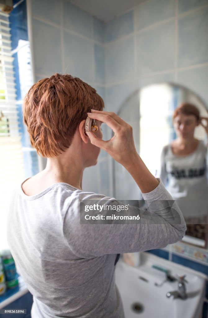 Women inserting hearing aid. Medical concept