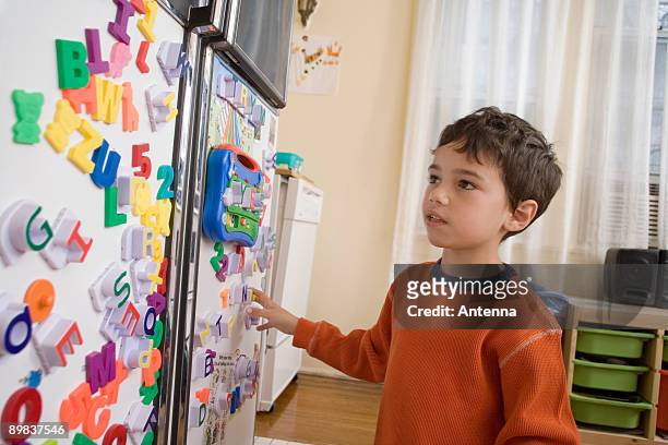 a young boy looking at toy magnets on a refrigerator door - bokstavsmagnet bildbanksfoton och bilder