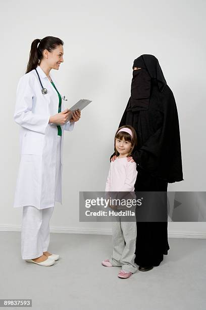 a doctor talking to a woman wearing a niqaab and her daughter - doctor stethoscope patient whole body stock pictures, royalty-free photos & images
