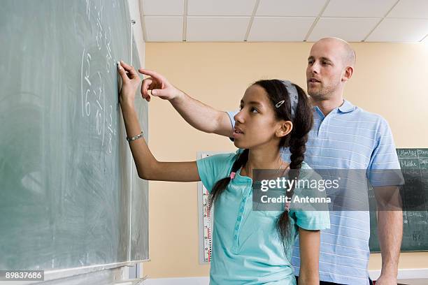 a girl writing on a blackboard with a teacher standing beside - two female teachers blackboard stockfoto's en -beelden