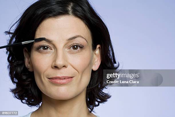 headshot of a woman applying makeup - sourcils photos et images de collection