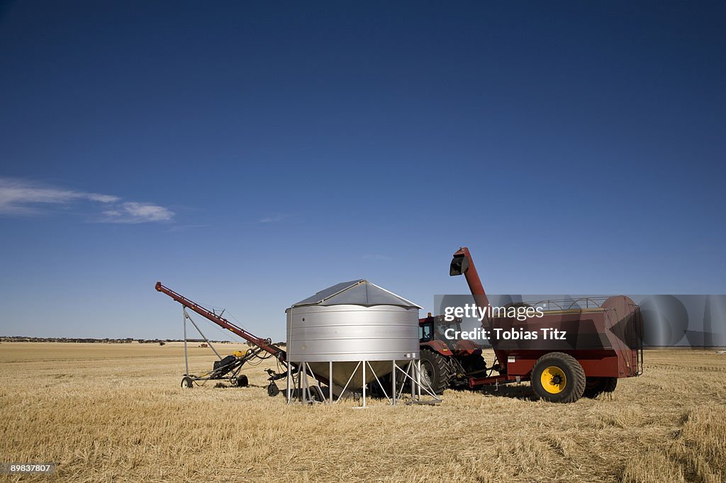 A tractor and combine next to a seed container in a wheat field