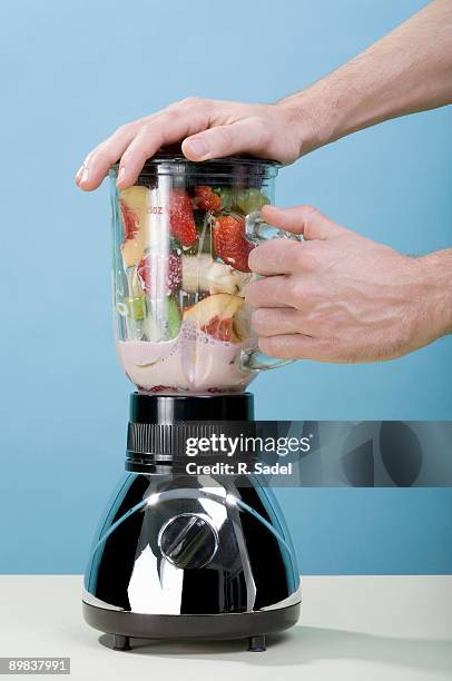 a human hand holding blender while it blends fruit - blender stock pictures, royalty-free photos & images