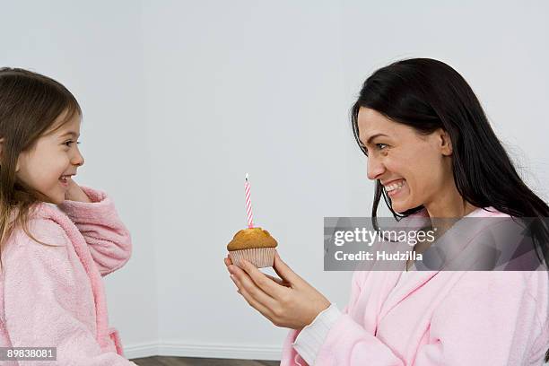 a mother giving her daughter a muffin with a candle in it - bathrobe stock pictures, royalty-free photos & images