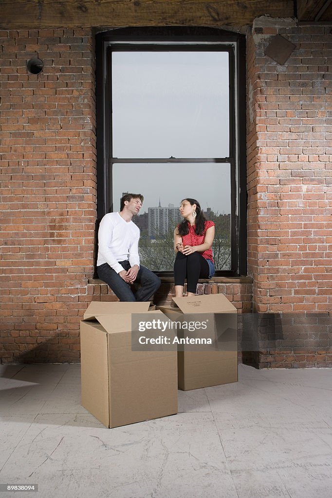 A couple sitting on the window sill with cardboard boxes