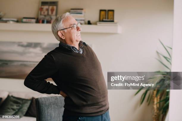 senior man in a living room having a packpain - leaning back stock pictures, royalty-free photos & images