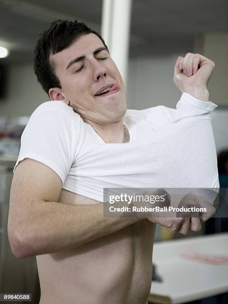 man putting on a shrunken t-shirt - 超小號 個照片及圖片檔