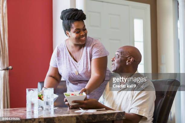 uomo anziano seduto a tavola, figlia adulta che serve cibo - african family eating foto e immagini stock