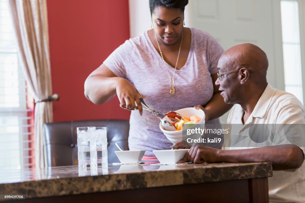 Senior man sitting at table, adult daughter serving food
