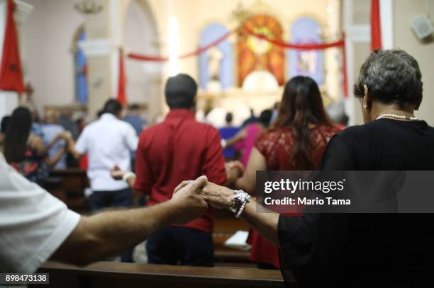 Faithful hold hands during 'midnight mass' at the Nuestra Senora Del Carmen Church on Christmas Eve on December 24, 2017 in Rio Grande, Puerto Rico....