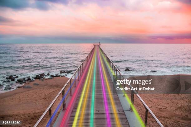 beautiful rainbow created with light trails with high speed over nice vanishing perspective of a pier going over the mediterranean sea with sunset colors in a creative picture. - high tech beauty stockfoto's en -beelden