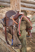 Western riding saddle and horse blanket on wooden corral post