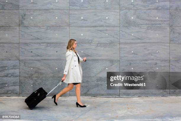 businesswoman with suitcase wearing trench coat - young woman trolley stock-fotos und bilder