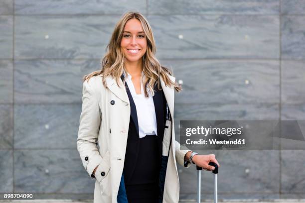 portrait of smiling businesswoman with suitcase wearing trench coat - trench coat stockfoto's en -beelden