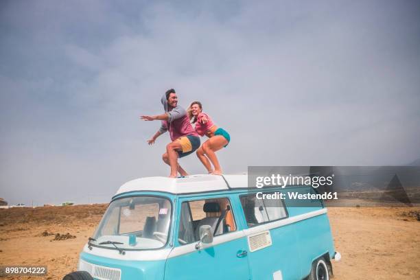 spain, tenerife, laughing young couple standing on car roof enjoying freedom - car photos stock-fotos und bilder