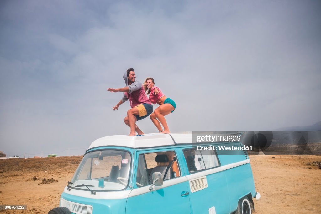 Spain, Tenerife, laughing young couple standing on car roof enjoying freedom