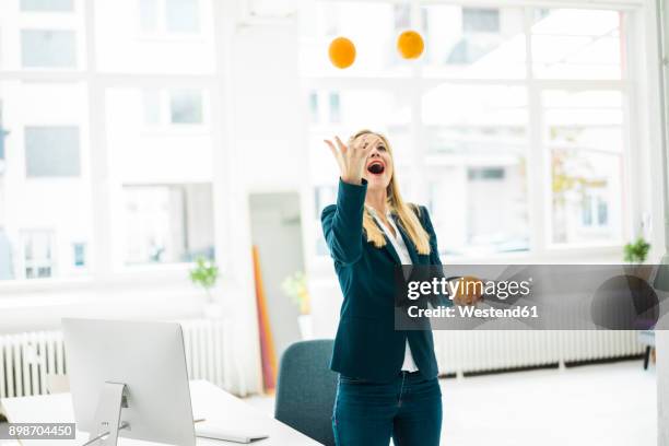 carefree businesswoman juggling with oranges in office - juggling stock pictures, royalty-free photos & images