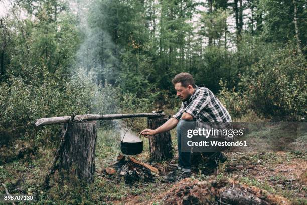 man cooking in cauldron in rural landscape - survival 個照片及圖片檔