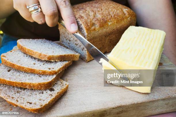 a person with a knife slicing through a block of butter for a sliced bread loaf. - untar de mantequilla fotografías e imágenes de stock