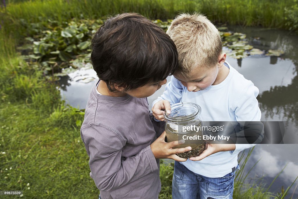 Two boys at pond, looking in fruit jar