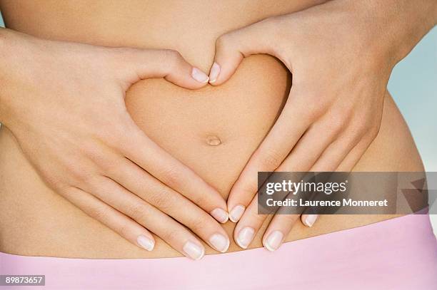 closeup on hands framing a heart on a woman belly - human abdomen ストックフォトと画像