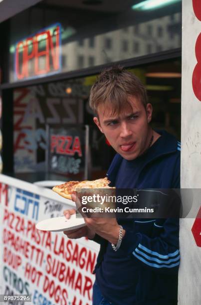 Singer Damon Albarn of English rock band Blur, eats a slice of pizza at a snack stand, circa 1995.