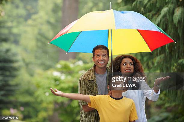 family sharing umbrella during rain shower - mother protecting from rain stockfoto's en -beelden