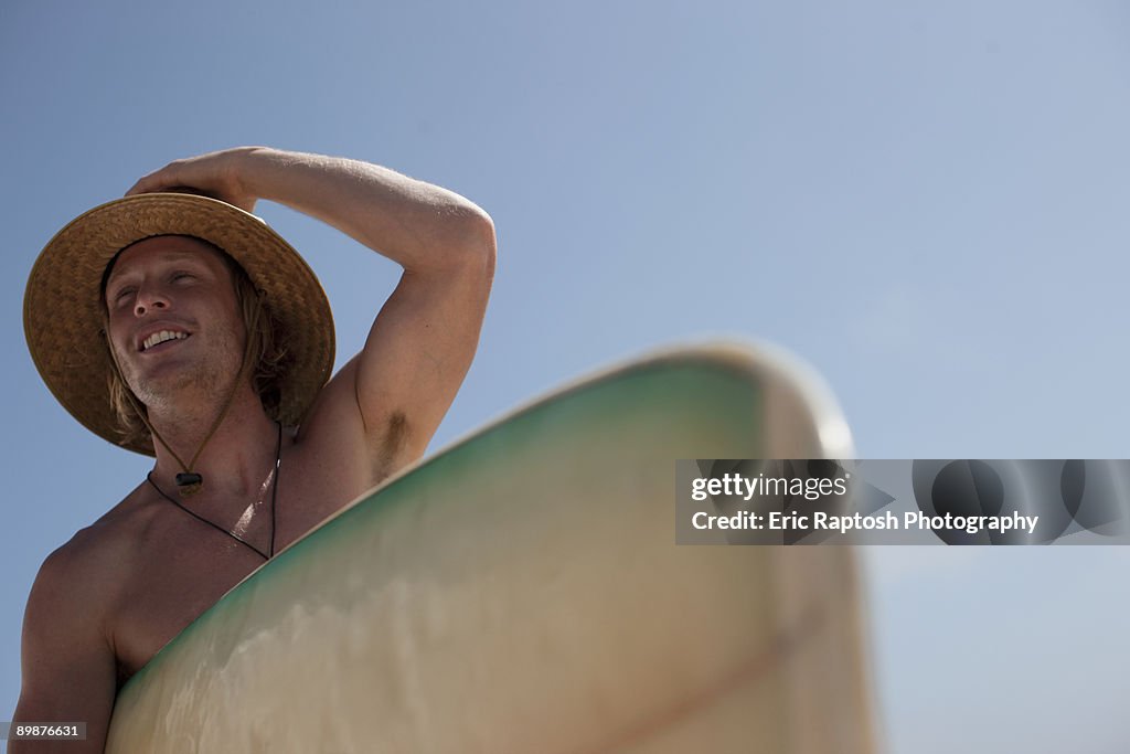 Man carrying surfboard holding hat