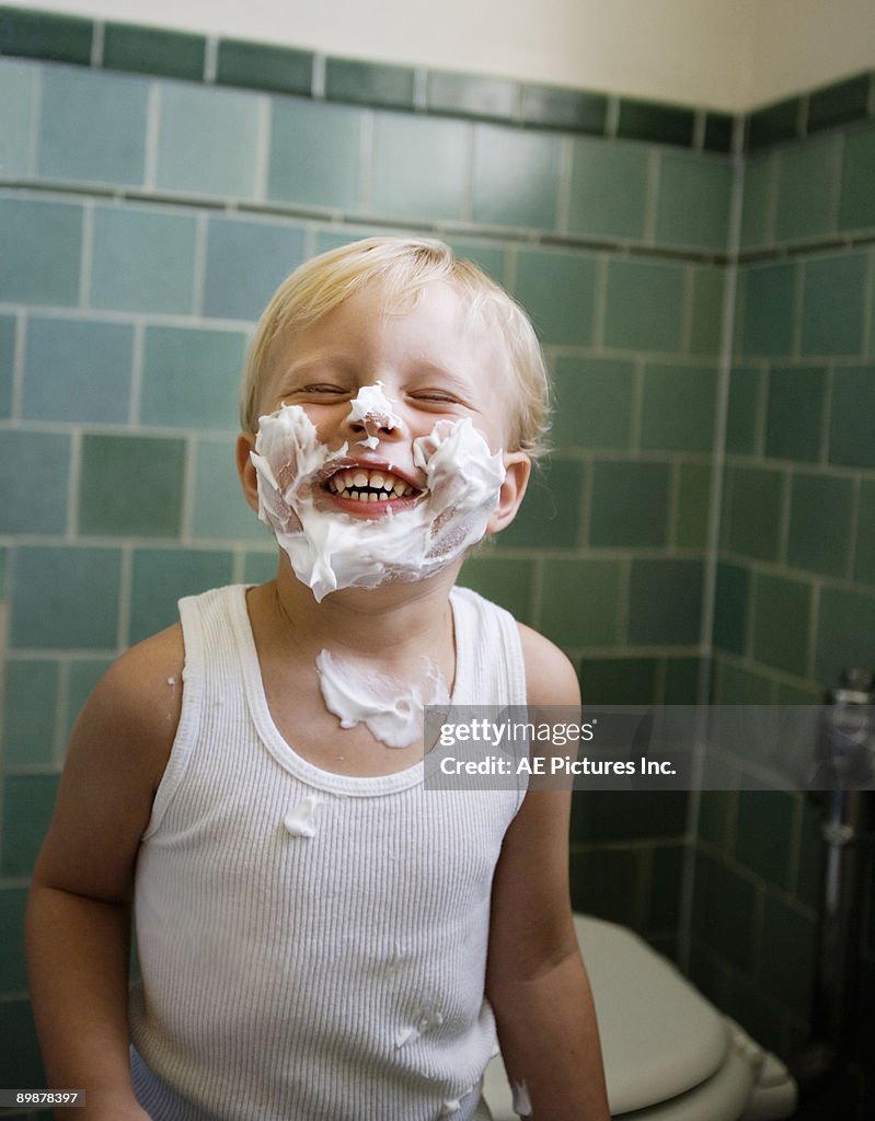 Toddler boy smiles with shaving cream on his face