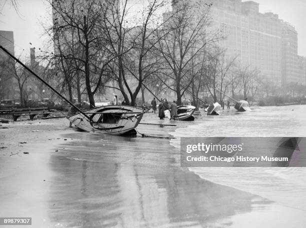 View of four boats lying on their sides on the shore of Lake Michigan at Belmont Harbor in Chicago, Illinois, after a storm, 1929. People are...