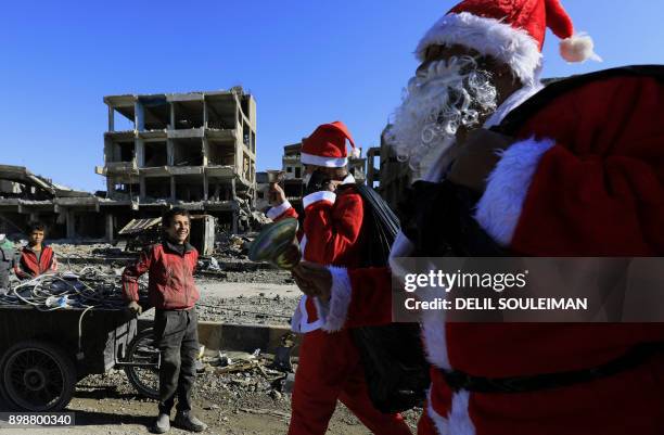 Syrian child smiles as men dressed in Santa Claus costumes walk past destroyed buildings in the eastern Syrian city of Raqa on December 26, 2017. A...