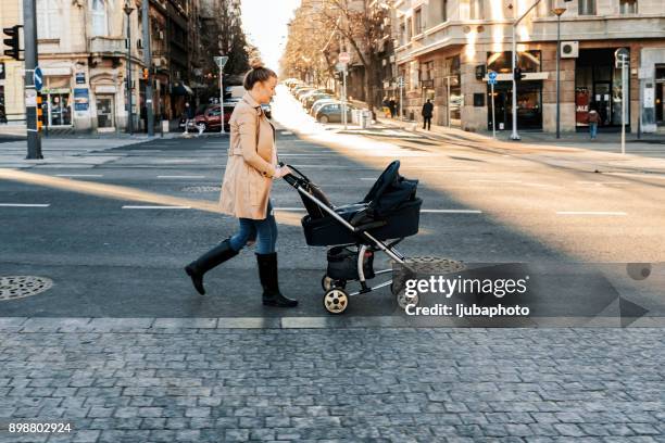 mother pushing a stroller in the street - mother stroller stock pictures, royalty-free photos & images