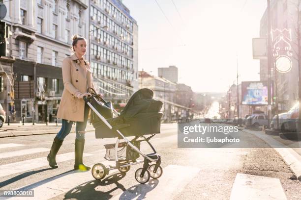 mother pushing baby stroller on lined pedestrian crossing - carrinho de criança imagens e fotografias de stock