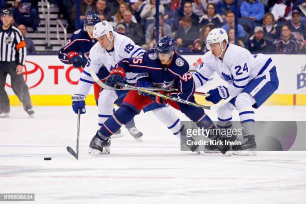 Lukas Sedlak of the Columbus Blue Jackets battles for control of the puck with Matt Martin of the Toronto Maple Leafs and Kasperi Kapanen of the...