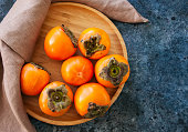 Fresh ripe persimmons on a wooden plate on a blue stone background