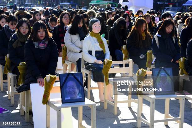 People sit around a statue of a "comfort woman" during an installation of empty chairs during a performance event, commemorating the death of eight...