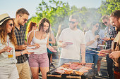 Group of people standing around grill.