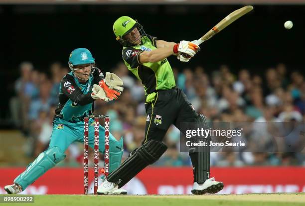 Sydney player Jos Butler hits the ball as Brisbane player Jimmy Peirson looks on during the Big Bash League match between the Brisbane Heat and the...