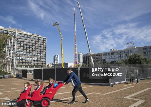 Man pushes a child stroller as he passes by a LEGO tower under construction in Tel Aviv's Rabin Square on December 27 as the city attempts to break...