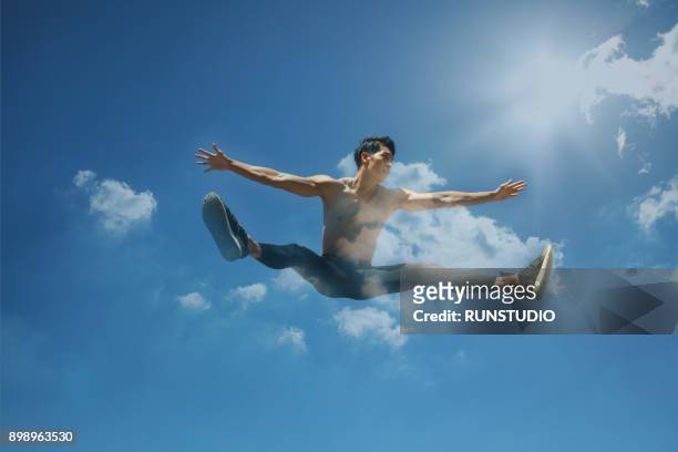 sport man jumping with blue sky and clouds on background - legs apart imagens e fotografias de stock