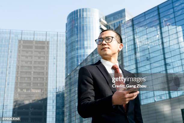 young businessman holding smartphone outside office building - businessman looking at map stock pictures, royalty-free photos & images