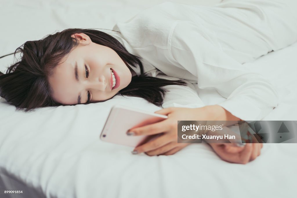 Smiling woman texting on cell phone on bed