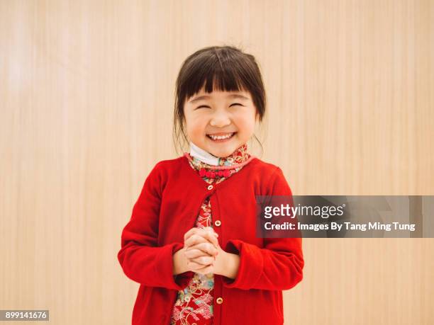 lovely little girl in chinese custom posing kung hei fat choy while smiling at camera joyfully.