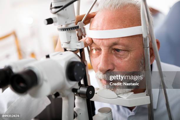 senior homme faire le test de la vue par un optométriste - eye test equipment stock photos et images de collection