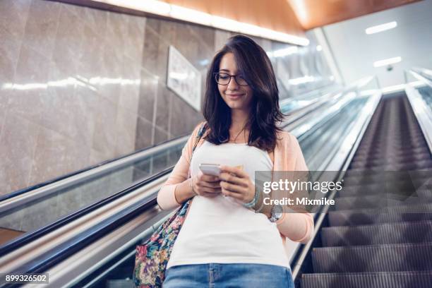 envoyer des sms sur son téléphone à l’intérieur de la station de métro femme - ascenseur interieur photos et images de collection