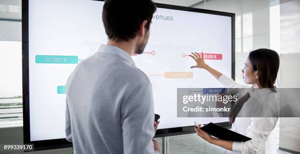 masculina e feminina colega discutindo esquemas financeiras na grande tela na sala de reuniões e a preparação para apresentação - monitor tátil - fotografias e filmes do acervo