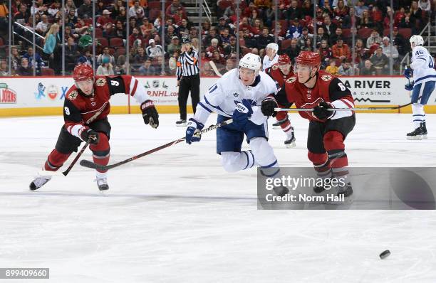 Zack Hyman of the Toronto Maple Leafs skates for a loose puck with Clayton Keller and Jakob Chychrun of the Arizona Coyotes during the first period...