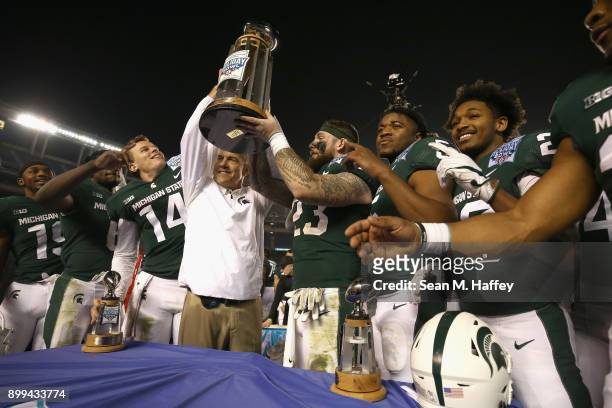 Head coach Mark Dantonio holds up the winning trophy along with players Chris Frey, Brian Lewerke, and Damion Terry of the Michigan State Spartans...